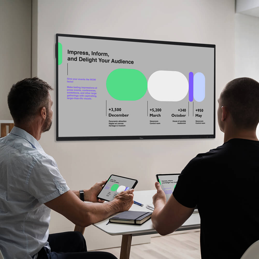 Two people in a small huddle room both with their laptops looking at a screen in front of them that is mirroring the same image through visual technology.